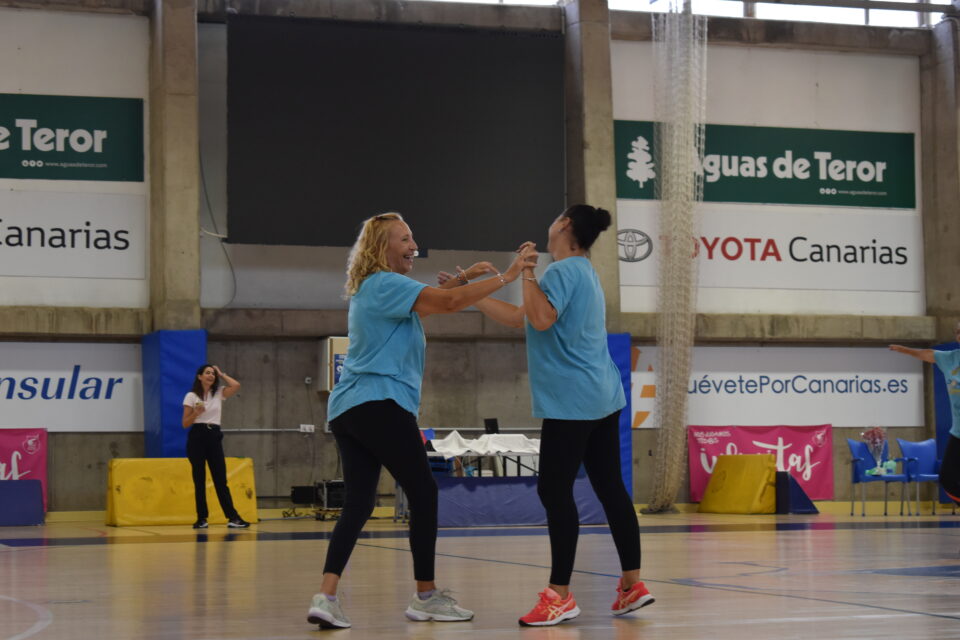 Dos mujeres sonrientes en camisetas azules disfrutan y se mueven en una cancha de baloncesto.