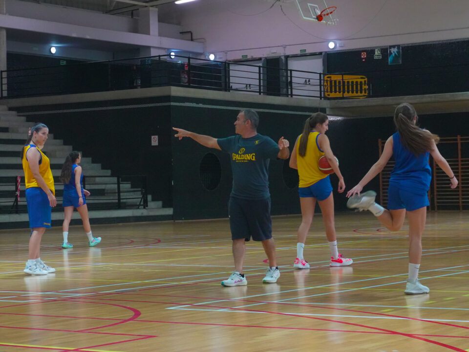 Entrenador dirige a jugadoras durante práctica de baloncesto en el gimnasio.