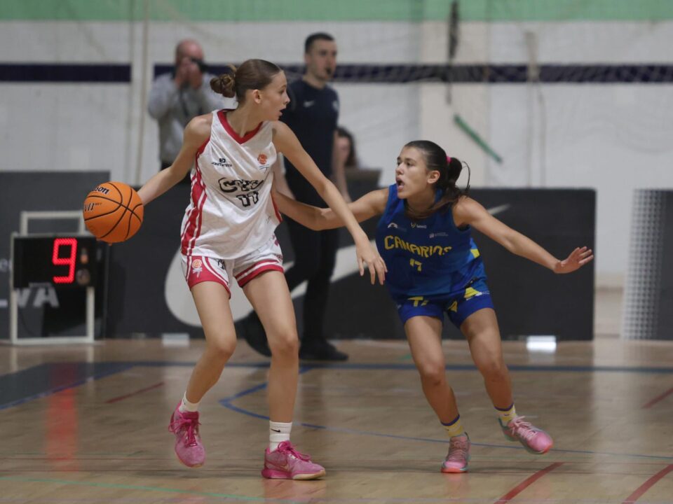  bronce autonómico con la selección de Canarias en el Campeonato de España",Jugadora con balón esquivando a una defensora en partido de baloncesto entre Canarias.