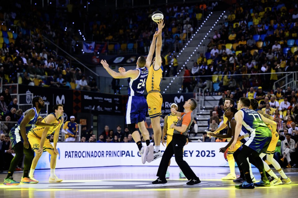 Jugadores saltan para el salto inicial en un emocionante partido de baloncesto.