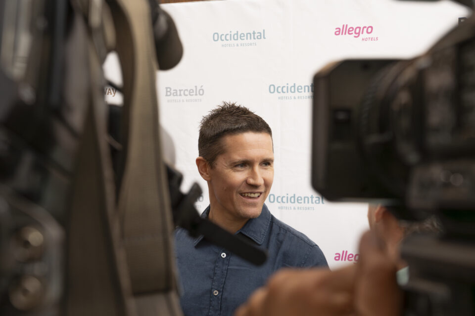 Jaka Lakovic sonriendo durante un evento, entre cámaras y un fondo promocional.