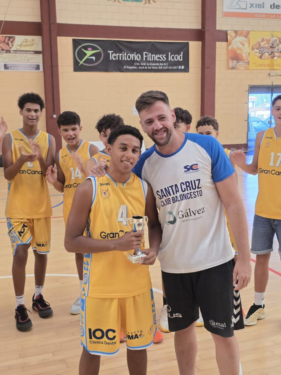 Niño con trofeo en mano posa con entrenador, celebrando un triunfo deportivo.